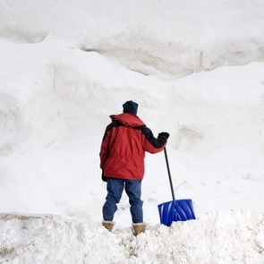 带雪铲的人面对大堆雪后视